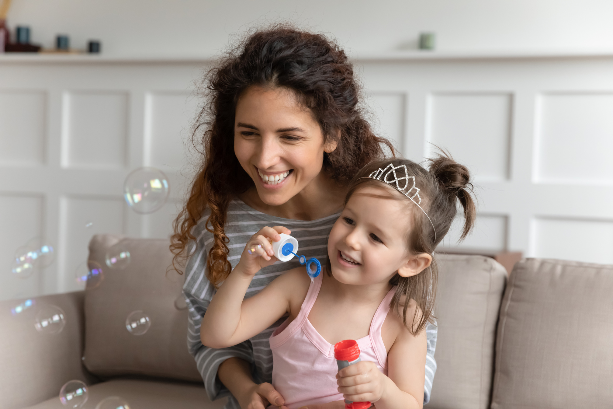 Pleasant young babysitter blowing soap bubbles with daughter.