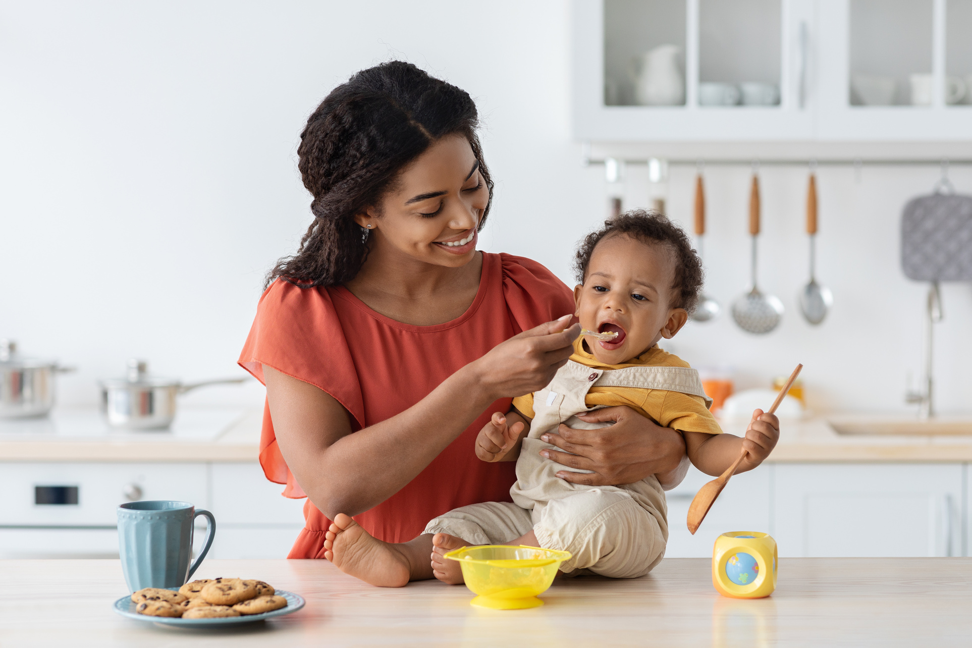 Childcare. Loving Black Mom Feeding Her Baby Son from Spoon in Kitchen